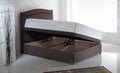 Picture of a side lift single ottoman in a white room with a brown headboard, a rug on the floor and a vase filled with white and black sticks to the side of it