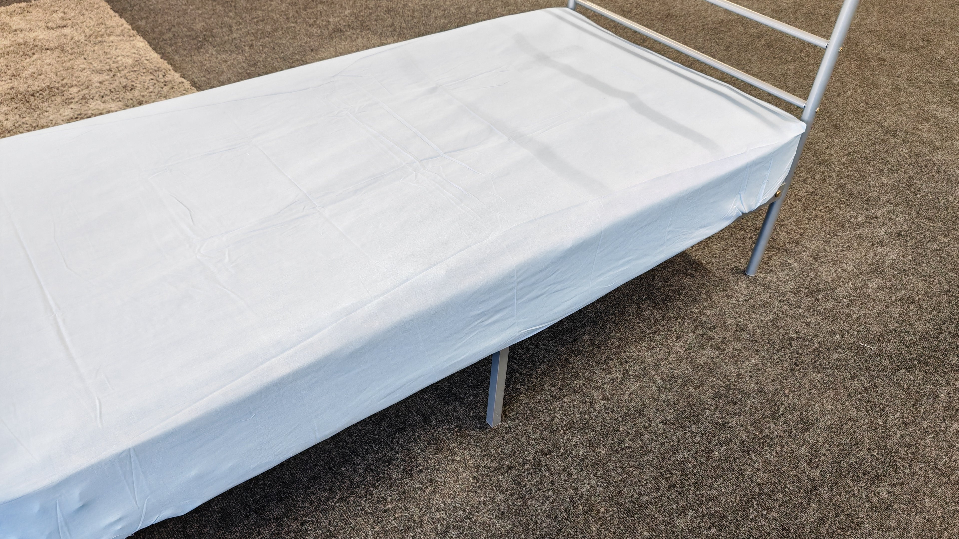 Picture of a light grey fitted sheet on a metal bed frame. 